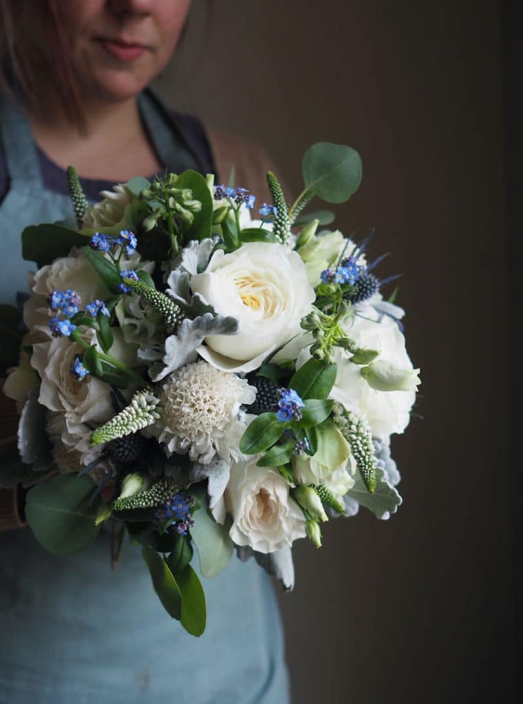 Image shows a florist at Green Parlour holding a spring wedding bouquet of David Austin roses, forget me nots, thistle and eucalyptus for a wedding at The Elephant Hotel, Pangbourne