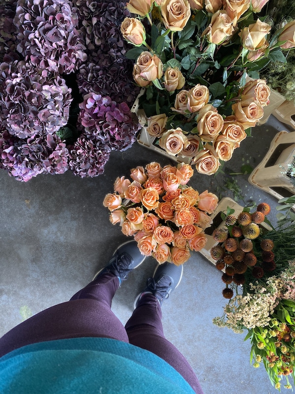 Image shows a womans legs wearing purple leggings, surrounded by pink, orange and peach flowers