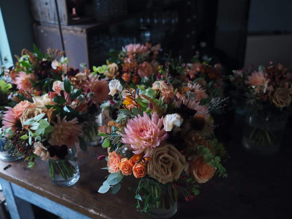 Image shows a wooden table filled with flower bouquets in pinks, oranges and peach