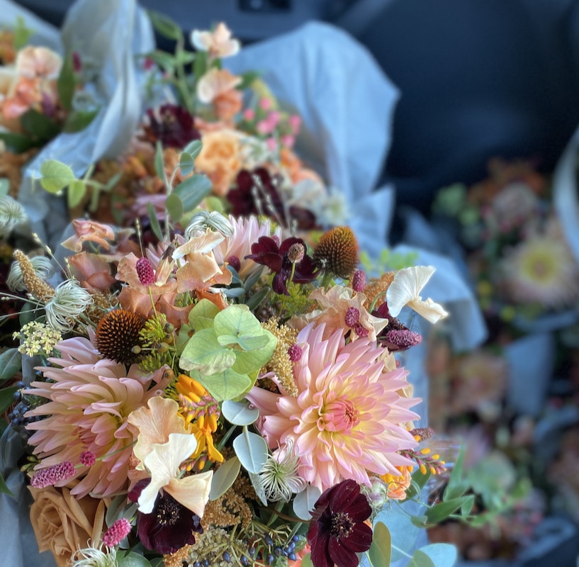 Image shows a selection of wedding flower bouquets in the footwell of a car. The flowers are pink dahlias.