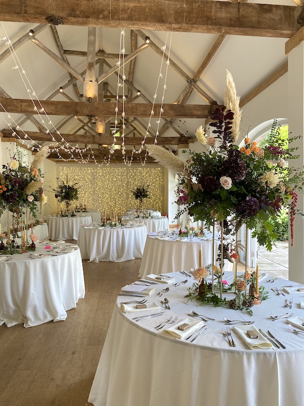 Image shows Dorney Court set up for a wedding, with round tables. The table have tall flower displays on them 