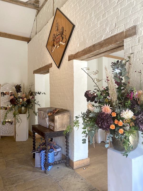 The image shows the entrance to Dorney Court wedding barn and is decorated with 2 white stands and 2 large arrangements of flowers in pinks, burgundy and peach.