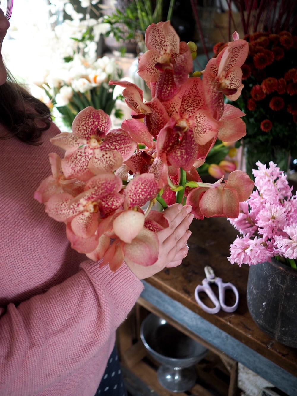 People holding flowers and scissors while creating arrangements in a floristry workshop